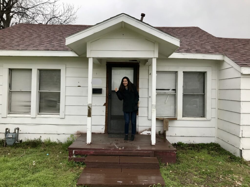 woman standing on porch of a small fixer upper house 