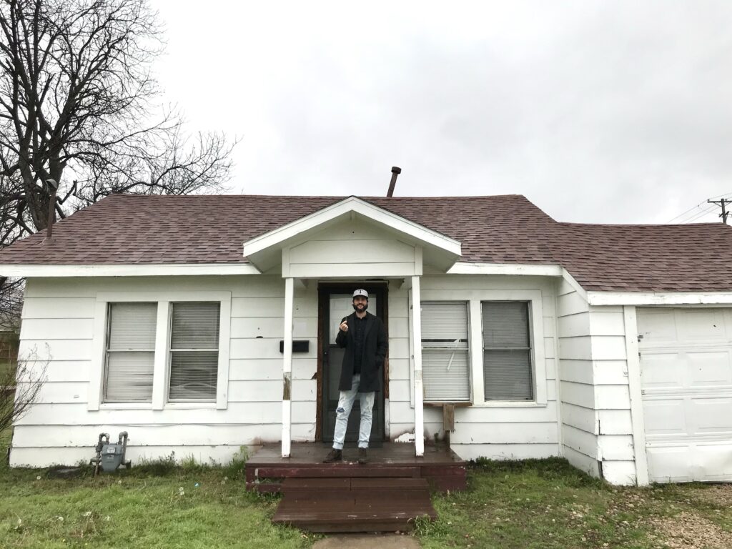 man standing in front of a small fixer upper house