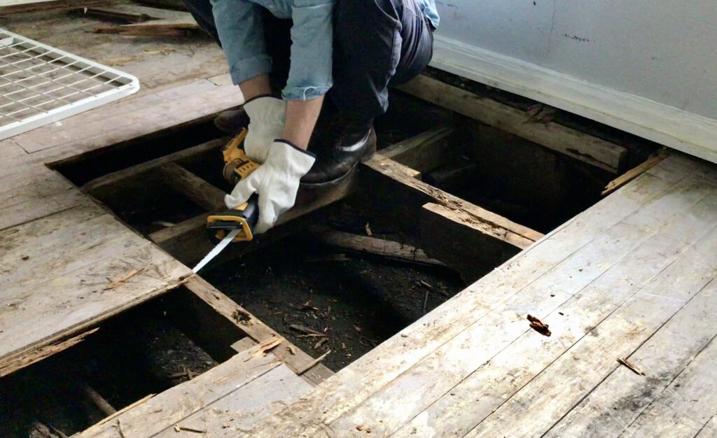 man using a reciprocating saw to pull up wood flooring 