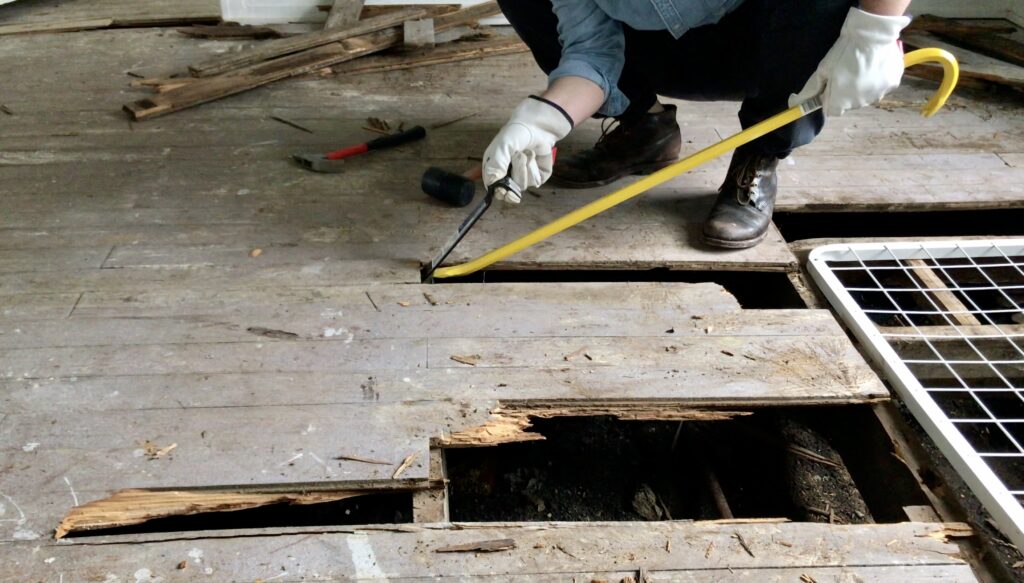 man using a pry bar to pull up wood flooring 