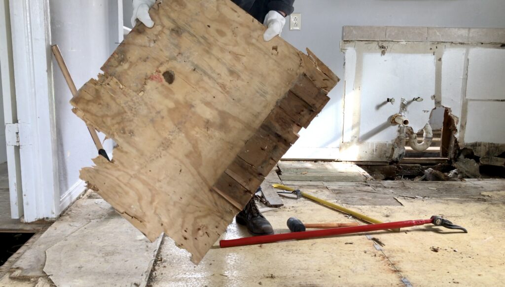 man removing linoleum and plywood flooring