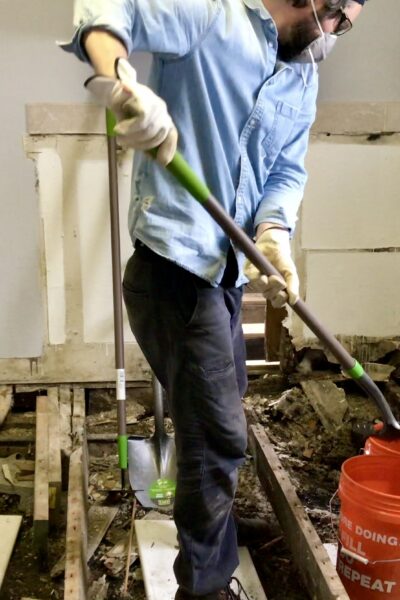 man shoveling dirt under flooring into bucket