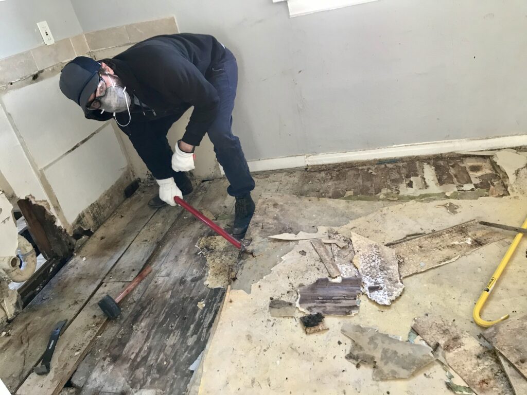 man pulling up several layers of old flooring in a kitchen