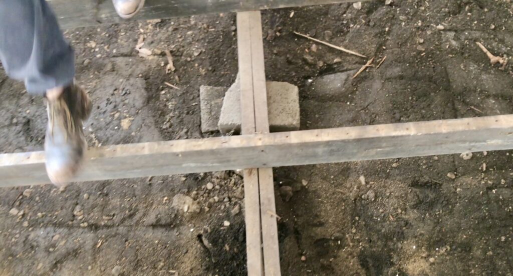 man's leg walking over sub flooring above dirt foundation
