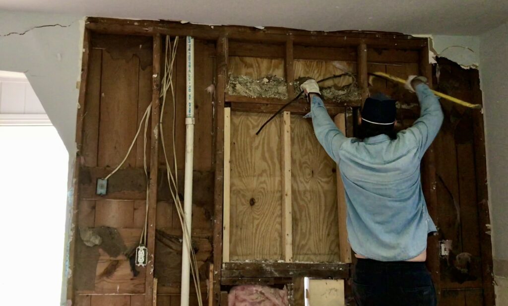 man pulling out wiring behind drywall and insulation