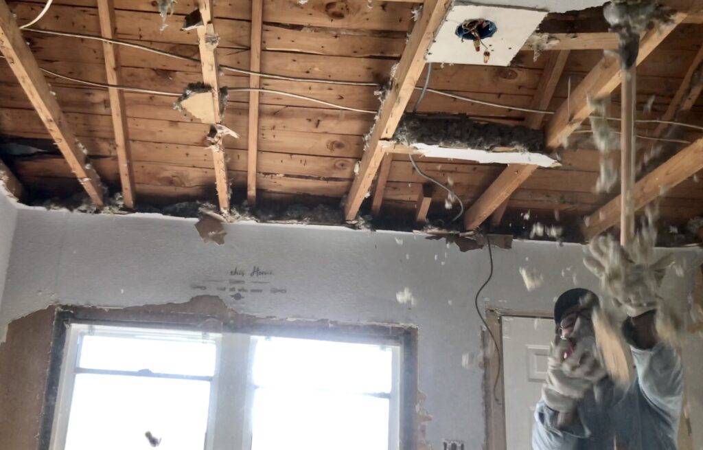 man removing ceiling drywall and insulation 