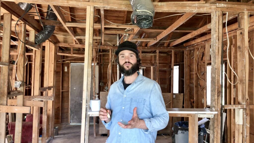 man looking at camera with exposed wood framing in fixer upper in the background
