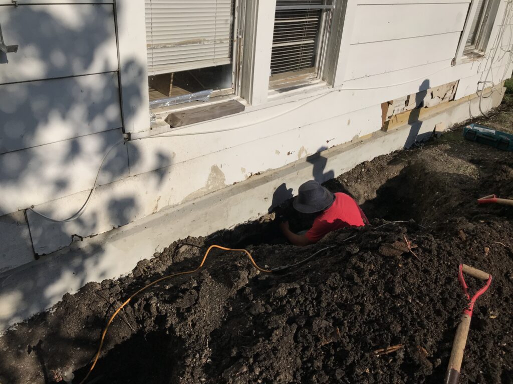 man digging foundation around small fixer upper house