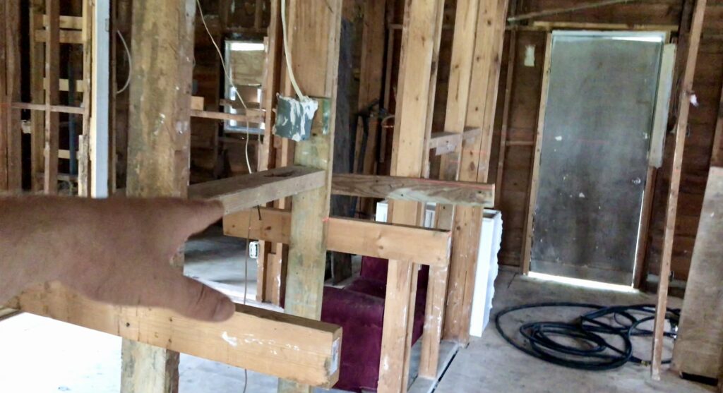 man's hand pointing toward wood frame in small fixer upper house 