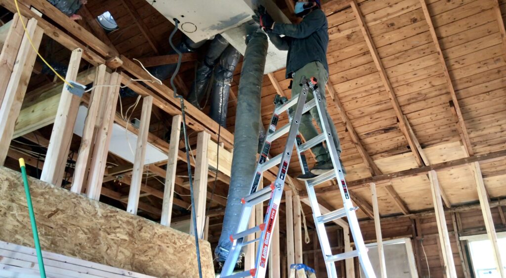 man removing heater unit on ladder near exposed vaulted ceiling 