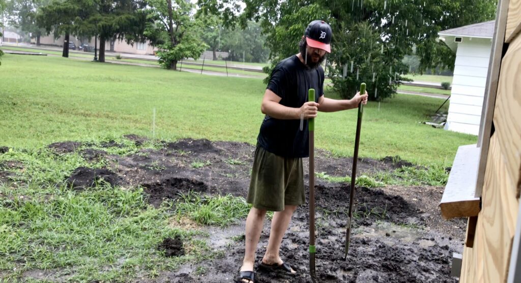 man outside shoveling dirt in rain