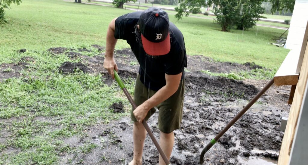 man outside shoveling dirt in rain