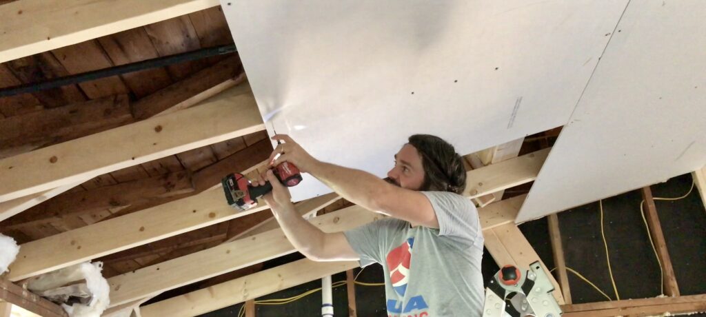 man screwing drywall into vaulted ceiling frame