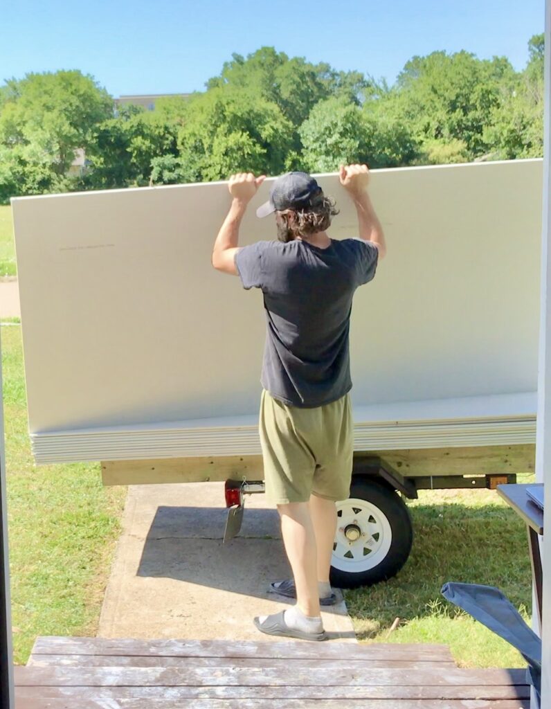 man lifting up drywall from car trailer