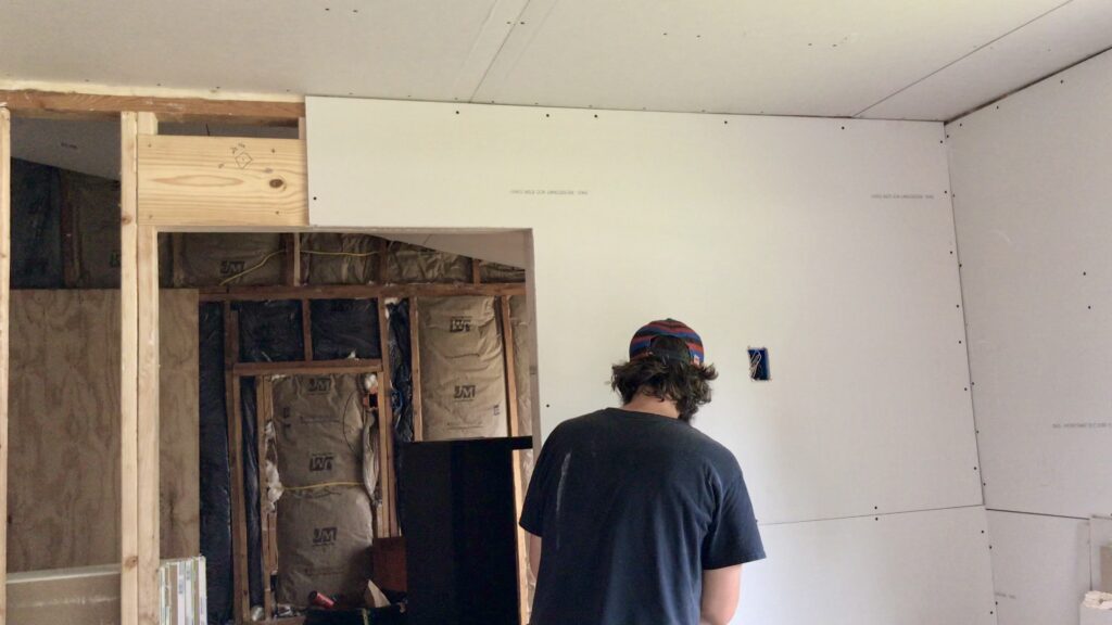 man hanging drywall with insulation in walls in background