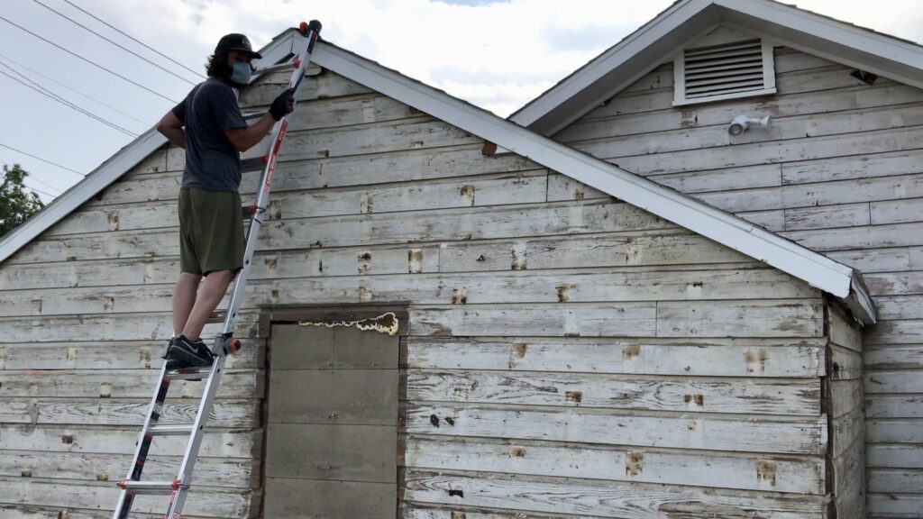 man on ladder removing siding to uncover old original wood siding