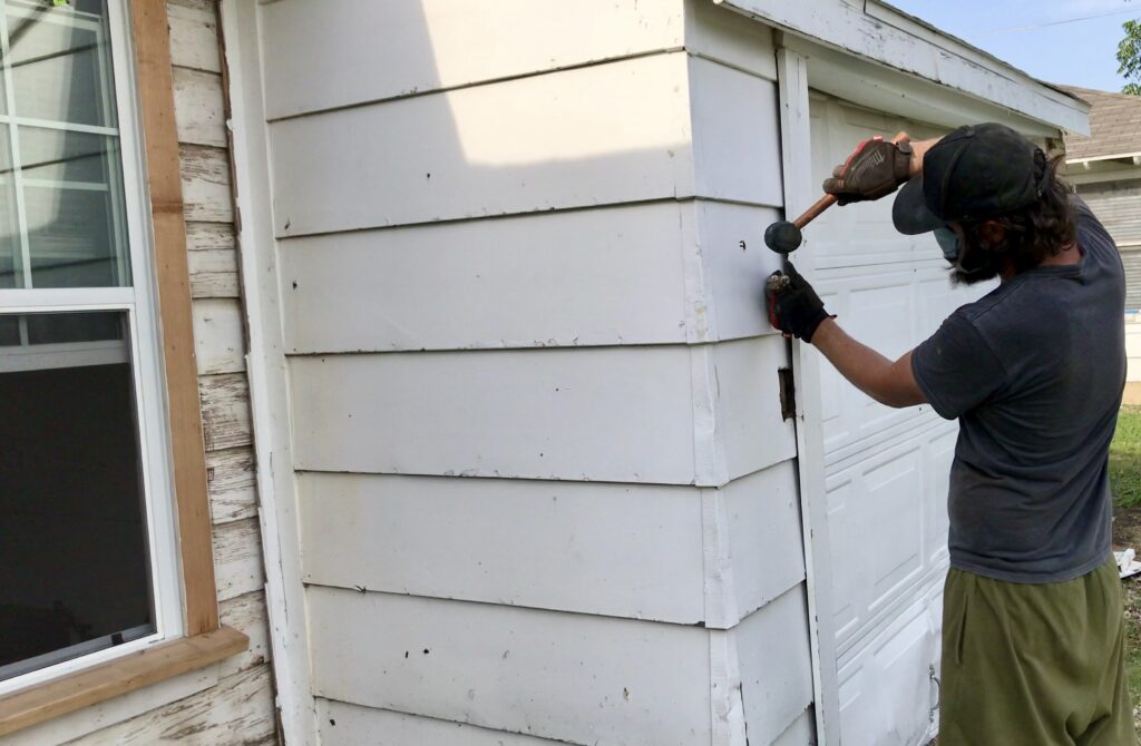 man removing garage trim with hammer and pry bar to uncover old original wood