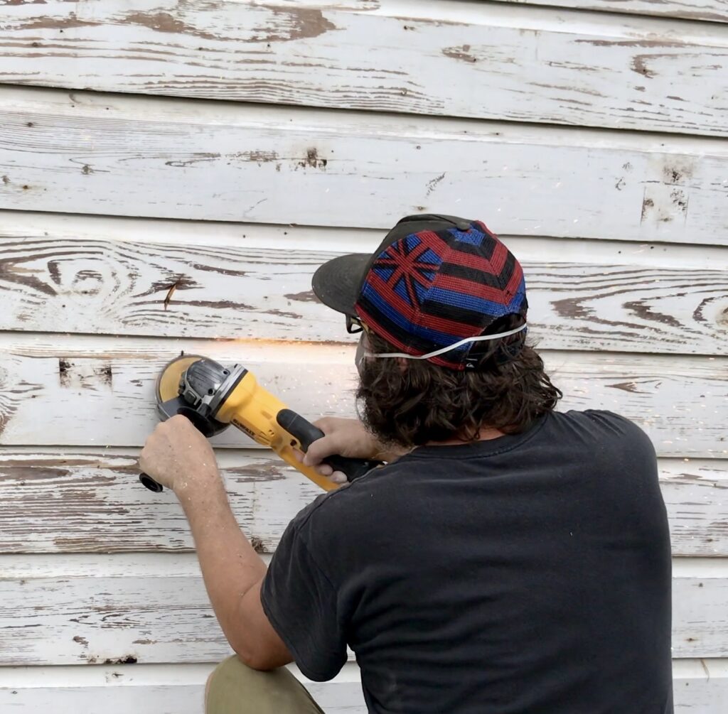 man using angle grinder to remove large nails from old cottage siding