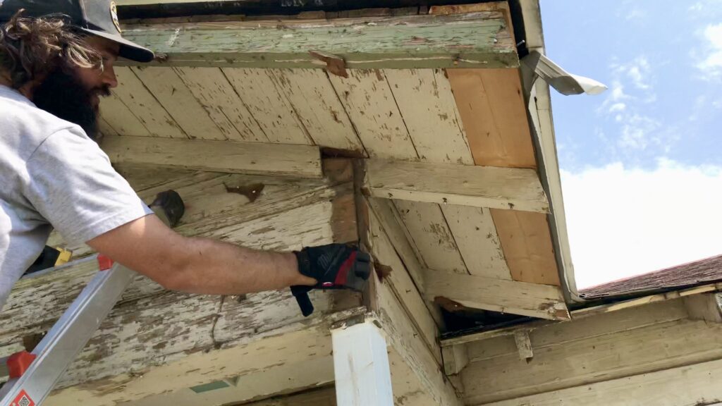 man on ladder touching siding trim under original green gable