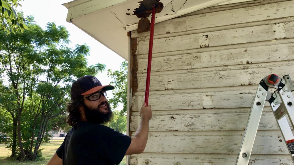 man with tool removing siding under soffit