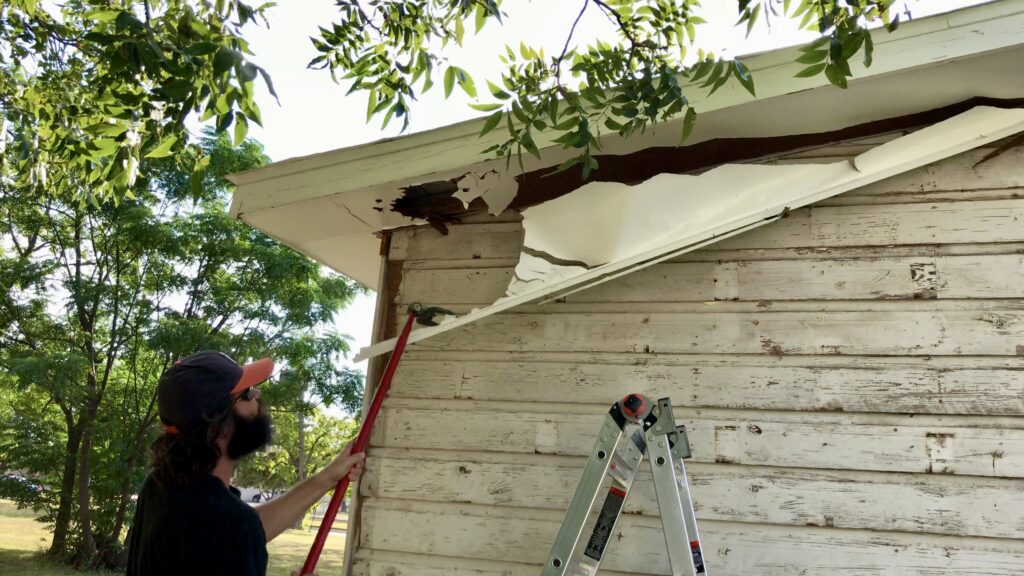 man with tool removing siding under soffit