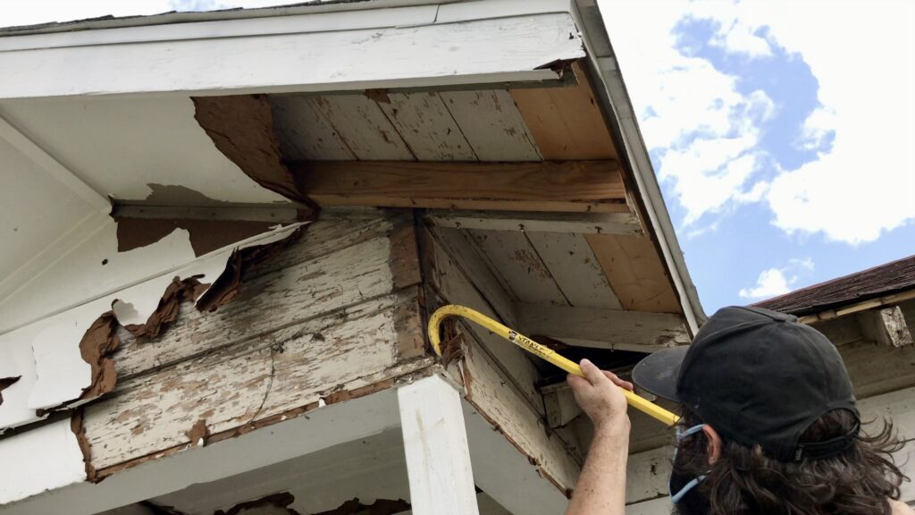 man using a crowbar to demo siding and remove it