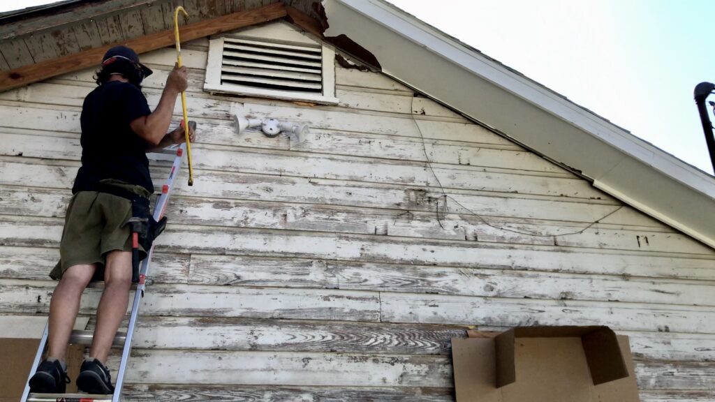 man on ladder removing stud on old cottage siding with pry bar 