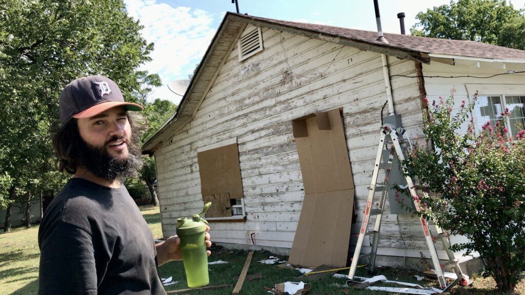 man with old cottage in the background with original siding exposed