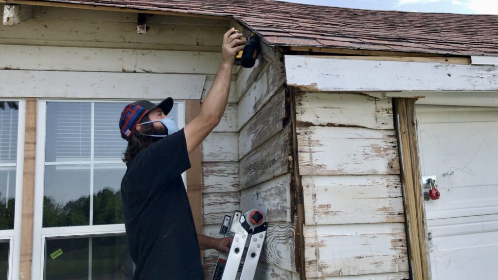 man sanding little white cottage with electric sander