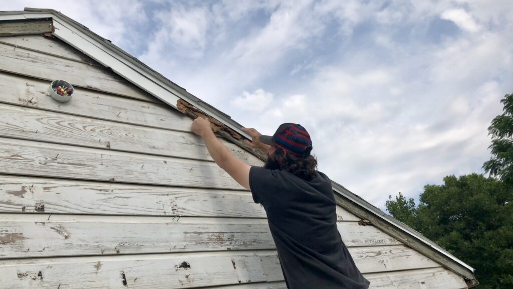 man removing old trim off cottage gable