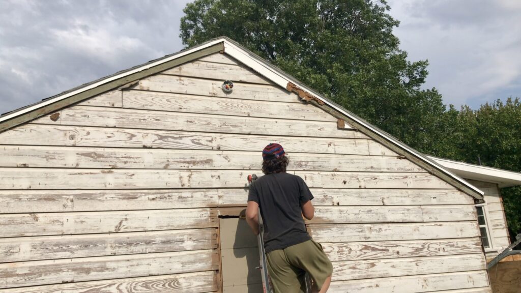 man on ladder facing old cottage siding