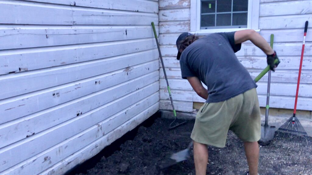 man digging dirt around cottage 