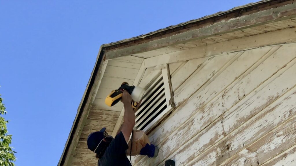 man spraying primer on old original cottage siding