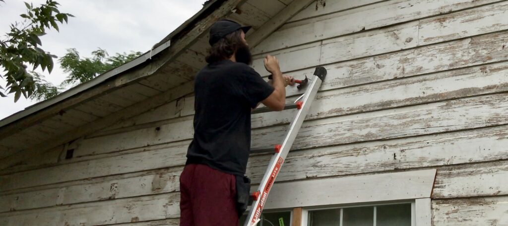 man pulling out nails from original siding on little cottage