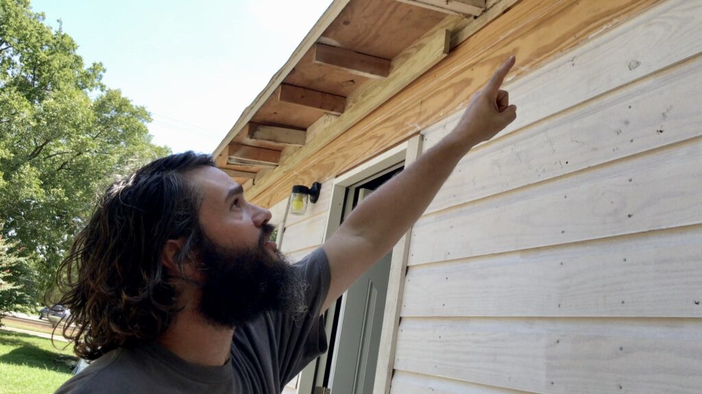 man pointing to cottage siding and original rafter tails