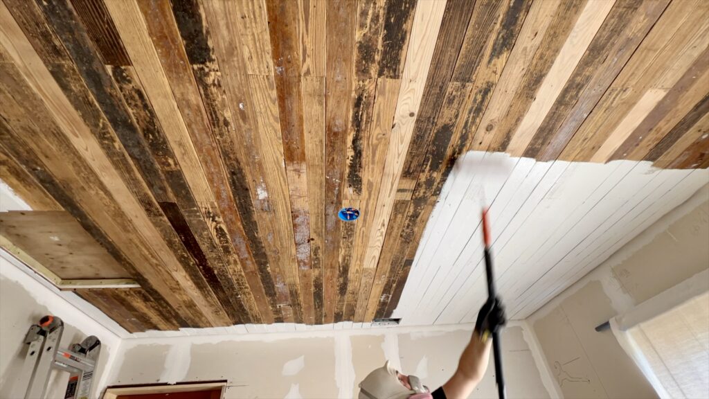 man priming reclaimed wood on ceiling