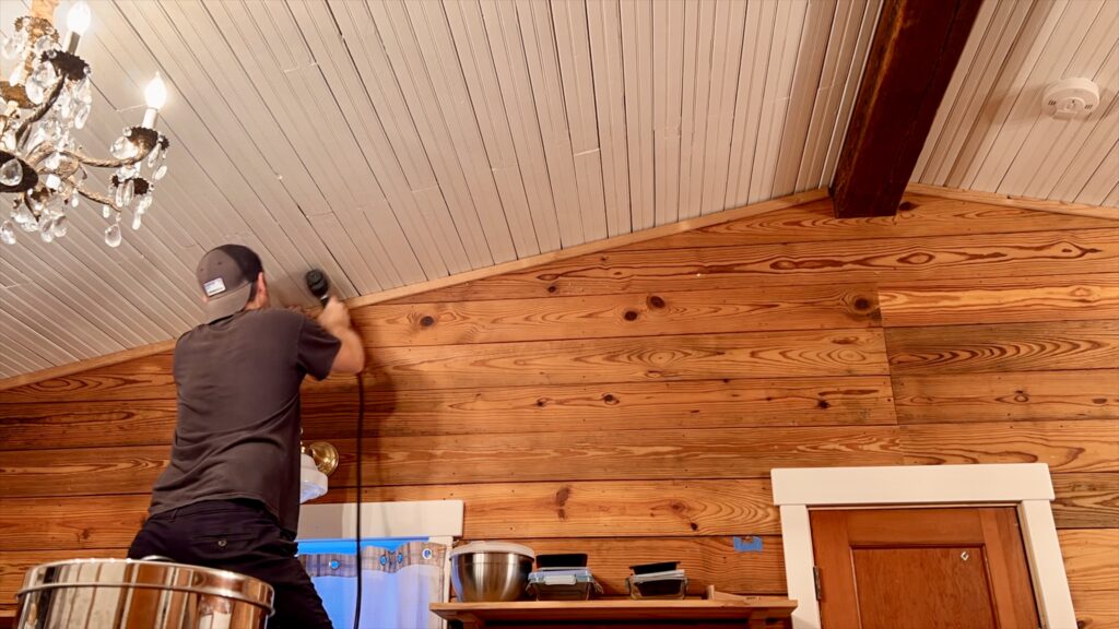 man installing custom trim for vaulted ceiling with antique chandelier hanging in background