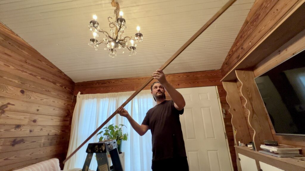 man holding custom trim for vaulted ceiling with antique chandelier hanging in background